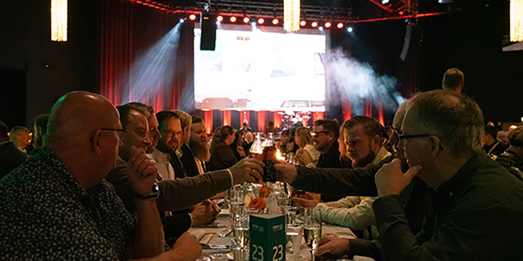 Book conference tickets: Persontrafik Industry Dinner, seated at long tables and toasting while entertainment takes place on stage in the background.