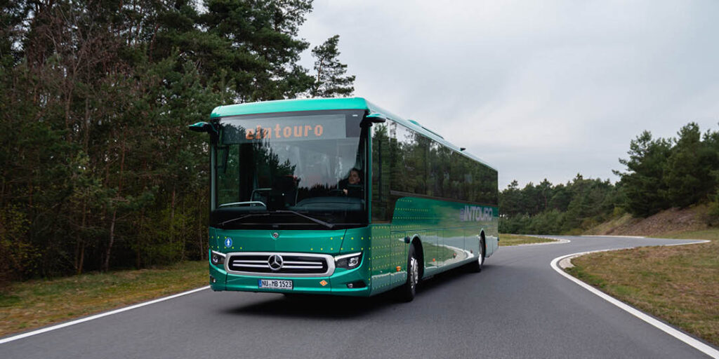 Grön Mercedes-Benz Intouro-buss kör på en slingrande väg genom ett skogsområde.
