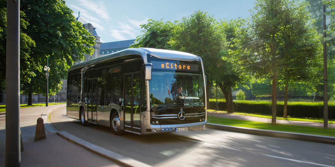 Daimler_1080x540px3 Electric Mercedes-Benz eCitaro bus from Daimler driving along a tree-lined city street.